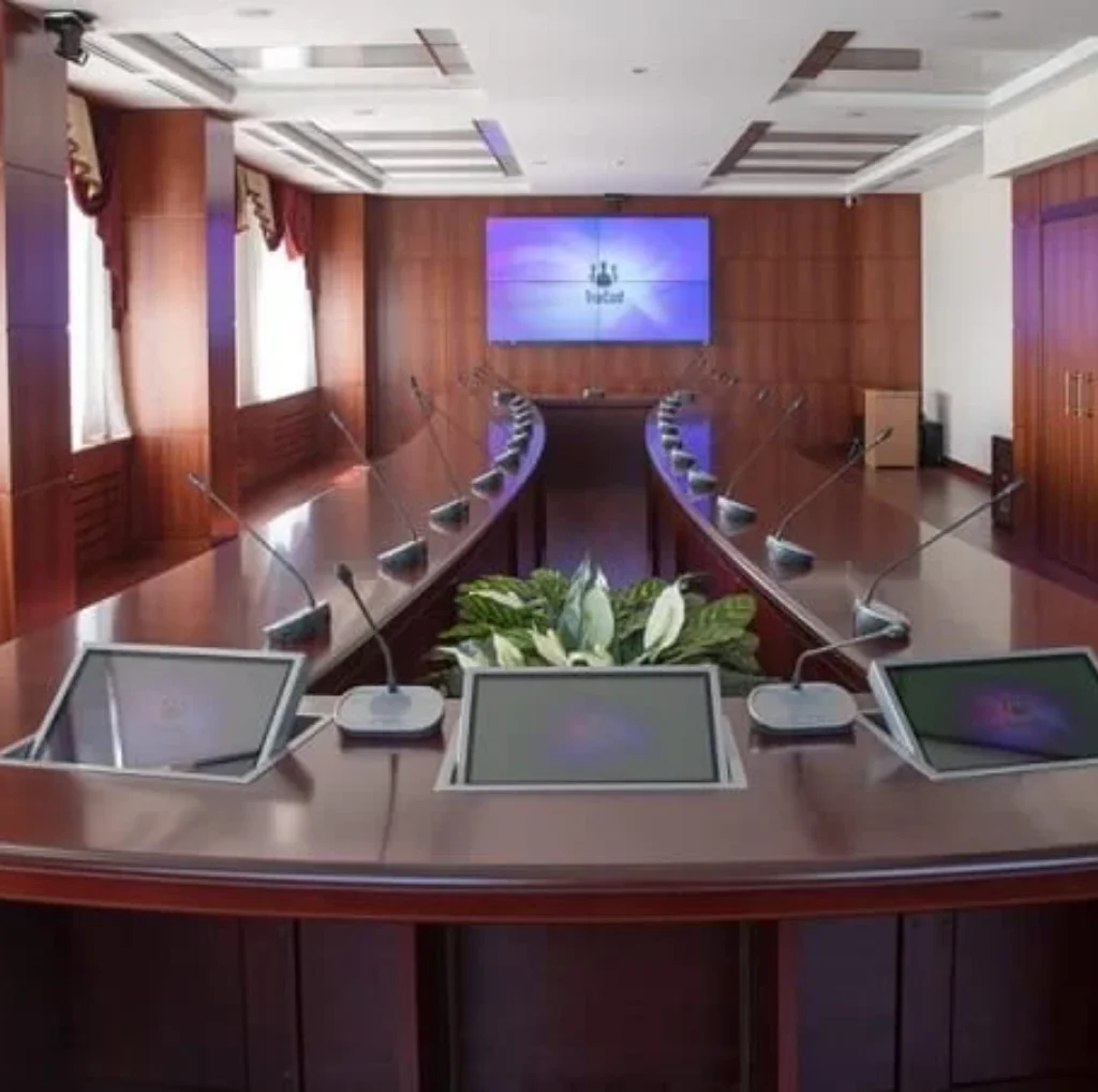 2x2 video wall screen on wall and large table with attached mics and small screens on tables for board room meetings.